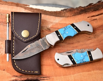 May include: A set of pocket knives with turquoise handles and a brown leather sheath. The knives have silver blades with intricate patterns. A sharpening tool is included.