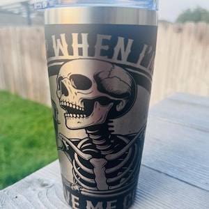 May include: A matte black stainless steel tumbler with a clear plastic lid. The exterior features a laser-engraved graphic of a skeleton holding a cup, with the text "WHEN I'M" visible at the top and "VE ME C" visible at the bottom of the design.