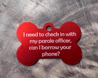 Peut inclure: Plaque rouge en forme d'os de chien avec un trou pour l'attache. Le texte blanc sur la plaque dit : « J'ai besoin de contacter mon agent de libération conditionnelle, puis-je emprunter votre téléphone ? »
