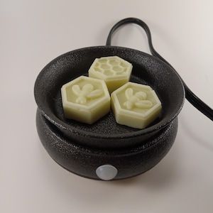 May include: A black electric wax warmer with a round dish and three white wax melts. The wax melts are shaped like honeycombs and have a bee design.