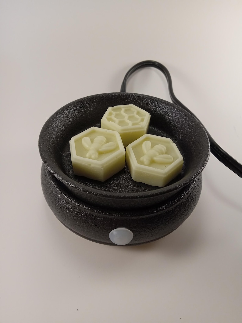 May include: A black electric wax warmer with a round dish and three white wax melts. The wax melts are shaped like honeycombs and have a bee design.