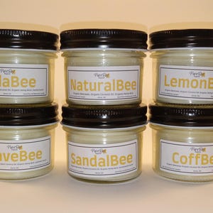 May include: Six glass jars with black lids containing candles. The labels on the jars read "NillaBee", "NaturalBee", "LemonBee", "LaveBee", "SandalBee", and "CoffBee".