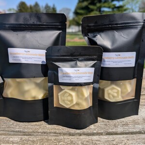May include: Three black resealable bags filled with white wax melts shaped like honeycombs. The bags have labels that say "Strawberry Lemonade Melts".