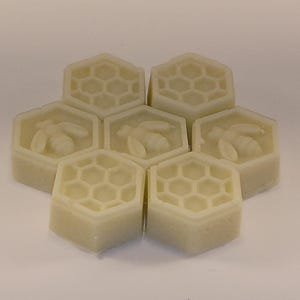 May include: Six hexagonal shaped soaps with a honeycomb pattern and a bee design. The soaps are a light beige color.