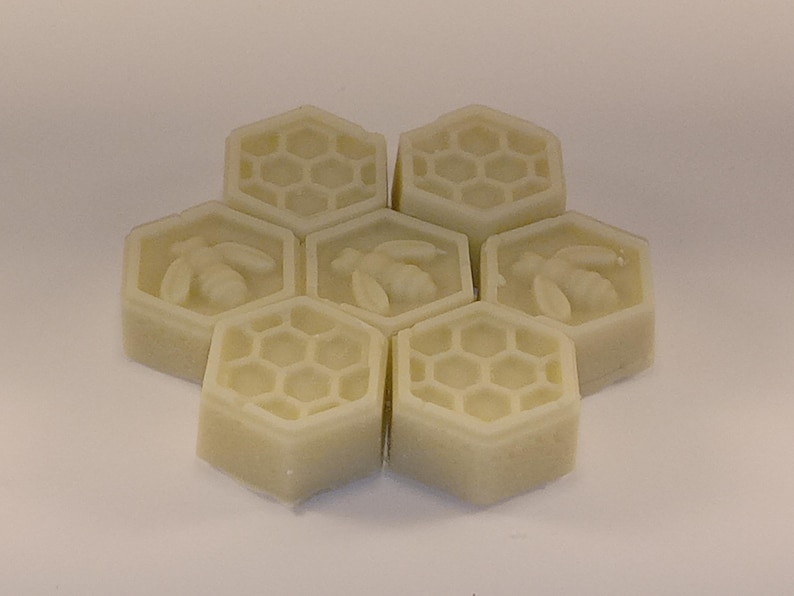 May include: Six hexagonal shaped soaps with a honeycomb pattern and a bee design. The soaps are a light beige color.