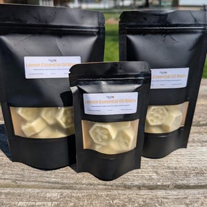 May include: Three black resealable bags with clear windows containing white wax melts. The bags are labeled "Lemon Essential Oil Melts".