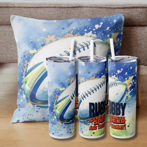 Könnte beinhalten: Zwei Edelstahlbecher mit einem blauen Aquarelldesign eines Rugbyballs. Die Becher haben den Aufdruck "Rugby Strength Speed and Teamwork".
