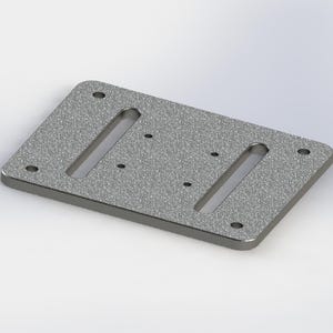 Op de afbeelding: Een rechthoekige, getextureerde, zilverkleurige metalen plaat met afgeronde hoeken. Het heeft twee langwerpige sleuven en vier cirkelvormige gaten, waarschijnlijk voor montage of bevestiging. Op een witte achtergrond.