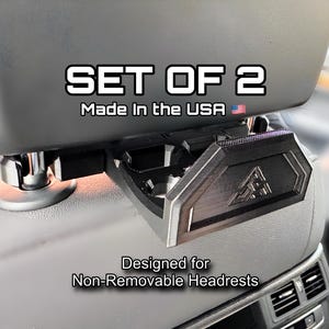 May include: A close-up of a car headrest with a black accessory attached. The text "SET OF 2" and "Made in the USA" are visible. The accessory is designed for non-removable headrests.