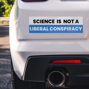Pode incluir: Um carro branco com um adesivo no pára-choques que diz "A ciência não é uma conspiração liberal". O adesivo tem uma faixa azul na parte superior.