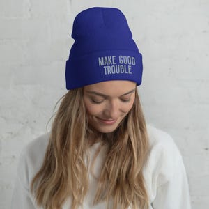 May include: A royal blue beanie with the text "MAKE GOOD TROUBLE" embroidered in silver on the front.