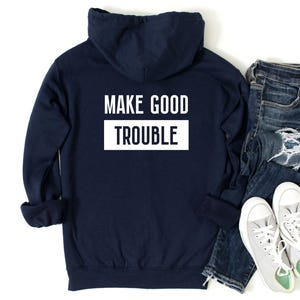 Può includere: Una felpa con cappuccio blu navy con la scritta "MAKE GOOD TROUBLE" stampata in bianco sul retro.
