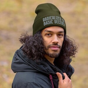 May include: A person wearing a dark green beanie with the text "Radicalized by Basic Decency" in white lettering.