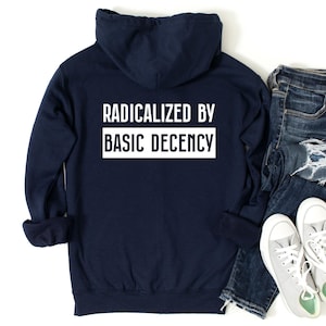Könnte beinhalten: Ein marineblauer Kapuzenpullover mit dem Text "Radikalisiert durch grundlegende Anständigkeit" in weiß auf der Rückseite.