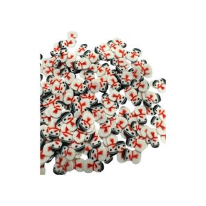 May include: A collection of small, flat, white snowman-shaped polymer clay slices. Each piece features a black hat, two black eyes, and a red scarf design. These decorative embellishments are scattered in a pile, showing uniform shapes and colors.