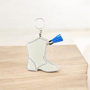 May include: A white cowboy boot keychain with silver glitter trim and a blue tassel. The keychain is attached to a silver metal ring. The boot shape is the focal point of this accessory.
