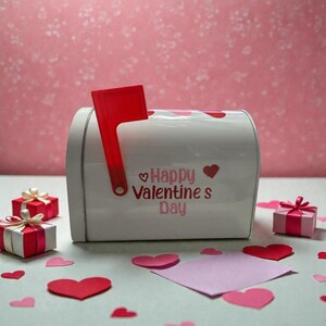 May include: A white mailbox with a red flag and the words "Happy Valentine's Day" in pink. The mailbox is decorated with red hearts. Small gift boxes and paper hearts are scattered around the mailbox.