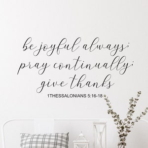 May include: White wooden bench with a black and white plaid pillow, two wicker baskets, and a white wall with a black calligraphy quote that reads "be joyful always, pray continually, give thanks 1 Thessalonians 5:16-18".