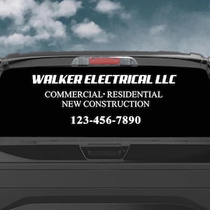 May include: Black pickup truck with a white decal on the rear window. The decal reads "WALKER ELECTRICAL LLC" above "COMMERCIAL • RESIDENTIAL • NEW CONSTRUCTION" and a phone number. The truck is parked on a dirt road.