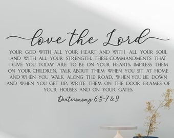 Può includere: Un muro bianco con un adesivo in vinile nero che recita "love the Lord" e include un versetto biblico da Deuteronomio 6:5-7&9. L'adesivo è sopra una cassettiera blu chiaro con una lampada bianca e oggetti decorativi in cima. Il testo "Sugar Creek" è visibile nell'angolo in basso a destra dell'immagine.