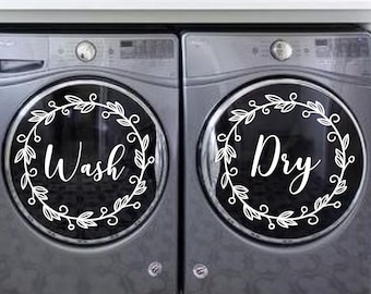Peut inclure: Deux machines à laver argentées avec des autocollants en vinyle blanc sur le devant. Les autocollants sont en forme de couronne avec les mots "Wash" et "Dry" à l'intérieur.