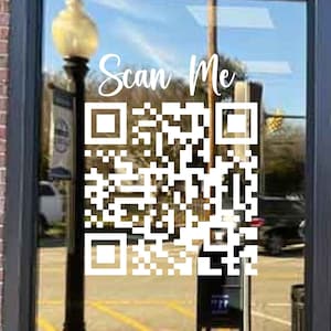 Op de afbeelding: Een witte QR-code met de tekst "Scan Me" erboven, op een glazen winkelruit. De tekst "Sugar Creek" staat onder de QR-code.