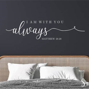 May include: A white wall decal with the text "I am with you always" and the scripture reference "Matthew 28:20". The decal is above a bed with a woven headboard and white bedding.