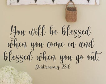 Può includere: Un muro bianco con un adesivo in vinile nero che recita "You will be blessed when you come in and blessed when you go out. Deuteronomy 28:6". Uno scaffale in legno bianco con un piccolo cestino intrecciato è appeso sopra l'adesivo. Un bouquet di ortensie bianche si trova su un tavolo in legno sotto l'adesivo. Il testo "Sugar Creek" è scritto in nero sul tavolo.