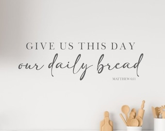 May include: A white wall with a gray vinyl decal that reads "Give us this day our daily bread Matthew 6:11". The decal is in a kitchen setting with a wooden countertop and a white sink.