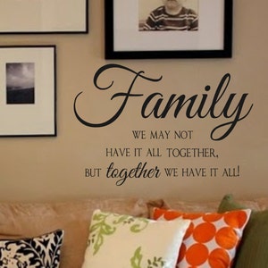 May include: A black and white wall decal with the text "Family We May Not Have It All Together, But Together We Have It All!" The decal is on a beige wall above a brown couch with pillows.