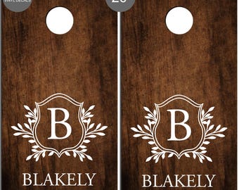 Könnte beinhalten: Zwei Cornhole-Spielbretter aus Holz mit dunkler brauner Oberfläche. Jedes Brett hat ein weißes Emblem mit dem Buchstaben "B", dem Namen "Blakely" und dem Jahr "EST. 2025". Die Bretter haben einen Durchmesser von 50.8 cm und ein Loch.