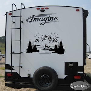 May include: Black and white silhouette decal of a mountain scene with a lake, trees, a deer, and a sun. The decal is on the back of a white camper with the text "Imagine Grand Design" and "Sugar Creek" on the camper.