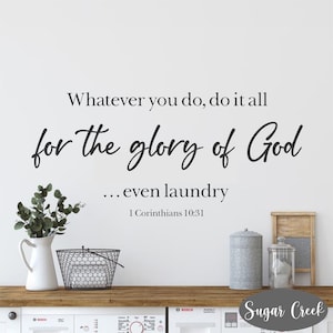 May include: A white wall with a black and white inspirational quote that reads "Whatever you do, do it all for the glory of God... even laundry 1 Corinthians 10:31". The quote is displayed above a wooden countertop with a white pitcher, a wire basket, and two metal canisters.