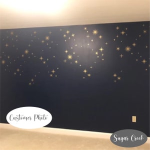 May include: A dark navy blue wall decorated with numerous gold star decals of varying sizes and shapes. The stars are scattered across the upper portion of the wall, creating a celestial pattern. A white oval label reads Customer Photo.