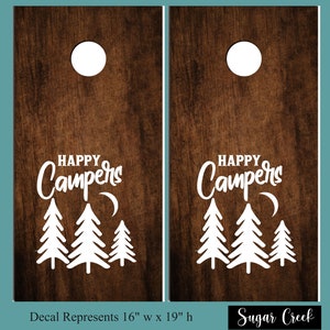 Op de afbeelding: Twee bruine houten cornhole-borden met een wit ontwerp. Het ontwerp bevat de tekst "Happy Campers" met een wassende maan en drie dennenbomen. De borden zijn 40,6 cm breed en 48,3 cm hoog. De tekst "Sugar Creek" staat onderaan de afbeelding.