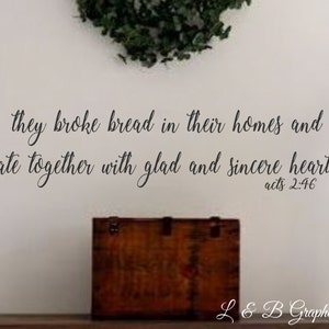 May include: A white wall with a black cursive quote that reads "they broke bread in their homes and ate together with glad and sincere hearts. acts 2:46". A wooden box sits on a shelf below the quote.