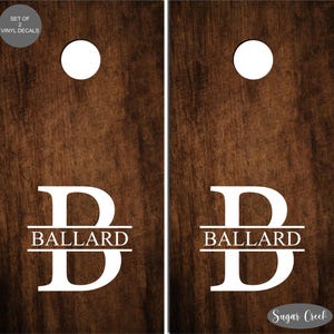 May include: Set of two wooden cornhole boards with a white letter "B" and the name "Ballard" printed on each board. The boards have a brown wood grain finish. The text "Sugar Creek" is printed on the bottom right corner of the boards.
