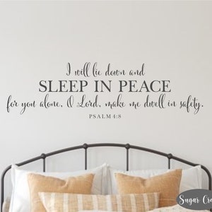 May include: A bedroom wall decal with the text "I will lie down and SLEEP IN PEACE for you alone, O Lord, make me dwell in safety. PSALM 4:8". The decal is above a black metal bed frame with tan and white patterned pillows.