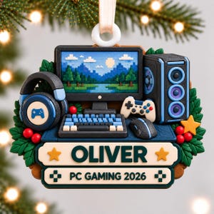 May include: A decorative Christmas ornament featuring a gaming PC setup with a monitor displaying a pixelated landscape, a keyboard, a mouse, a controller, and headphones. The base includes the name OLIVER and the text PC GAMING 2026.