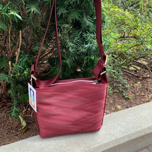 May include: A maroon crossbody bag made from repurposed seatbelt material. The bag has a zipper closure and a long adjustable strap.