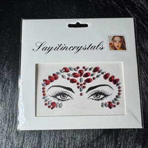 May include: A face jewel sticker set featuring a design of eyes with long eyelashes, surrounded by red and silver rhinestones. The package has the text "Sayitincrystals".