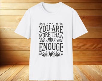 以下が含まれることがあります： 白いTシャツに、黒いグラフィックで「You are more than enough」と書いてあり、花柄とハートのデザインが施されています。