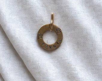 Peut inclure: Une médaille de chien circulaire dorée avec le nom "BONNIE" estampé au centre. Deux empreintes de pattes sont estampées sur la médaille. Elle possède une petite boucle en haut pour l'attacher au collier.