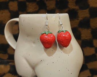 May include: A pair of silver dangle earrings with red and green strawberry charms.