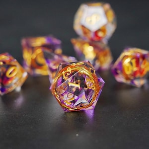 May include: A set of seven polyhedral dice with a clear, faceted design. The dice feature purple and gold accents, with gold numbering. The dice are designed for tabletop role-playing games.