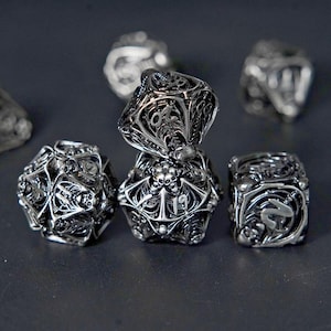 May include: Close-up of several silver, intricately designed dice. The dice feature detailed patterns, including skulls and ornate filigree. The dice are arranged on a dark surface, with some in focus and others blurred.