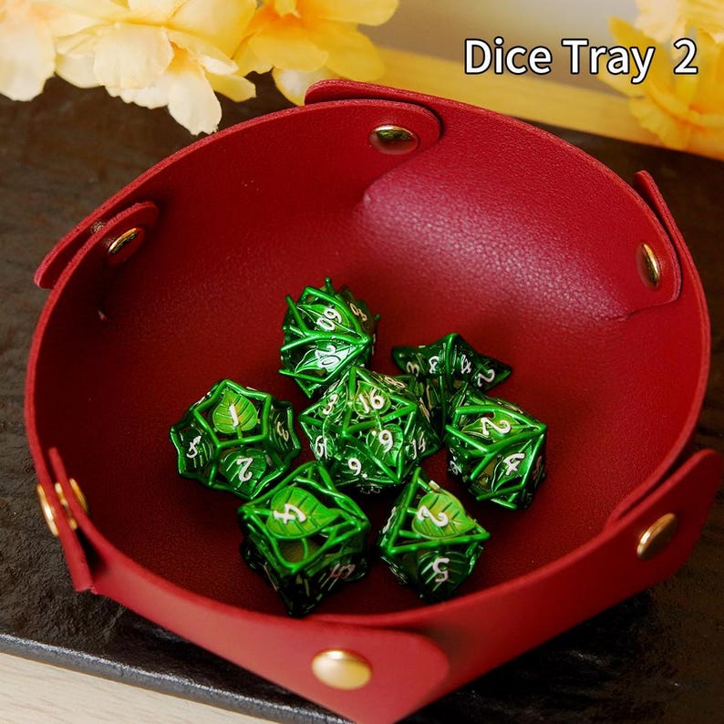 May include: A red leather dice tray with gold rivets contains several green metal dice. The dice feature a leaf design and white numbers. The text "Dice Tray 2" is visible in the upper right corner.
