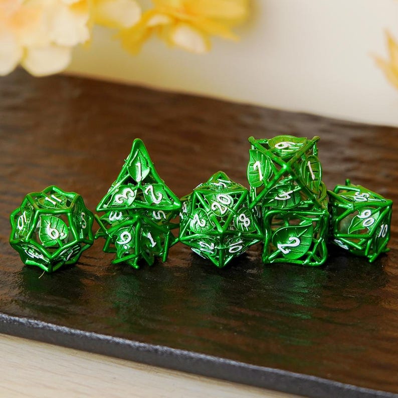 May include: A collection of six green metal dice featuring a leaf design. The dice are in different geometric forms, such as a d4, d6, d8, d10, d12, and d20. The numbers are white and clearly visible.