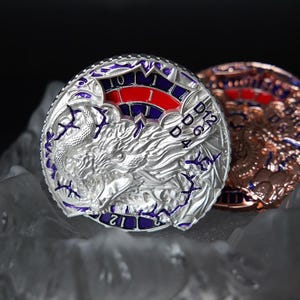 May include: Two detailed coins, one silver and one bronze. The silver coin has a dragon design with purple detailing and a red and white section with numbers. The bronze coin shows a similar design. The coins are set on a textured surface.