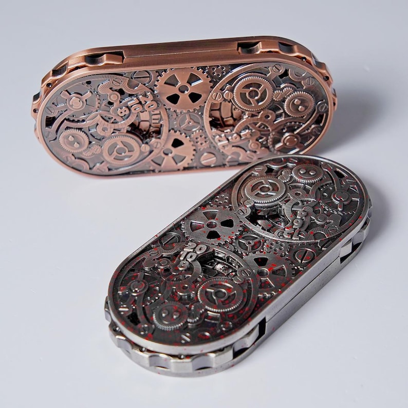 May include: Two steampunk-style metal cases with intricate gear designs. One case is copper-colored, the other is silver with red accents. The cases are oval-shaped and feature detailed mechanical components.